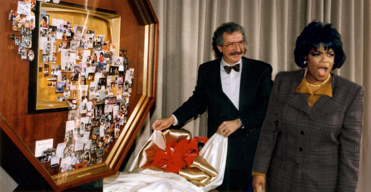 Artist Lawrence Romorini unveiling large shadow box collage for Oprah Winfrey, who is standing next to the art with jaw dropped