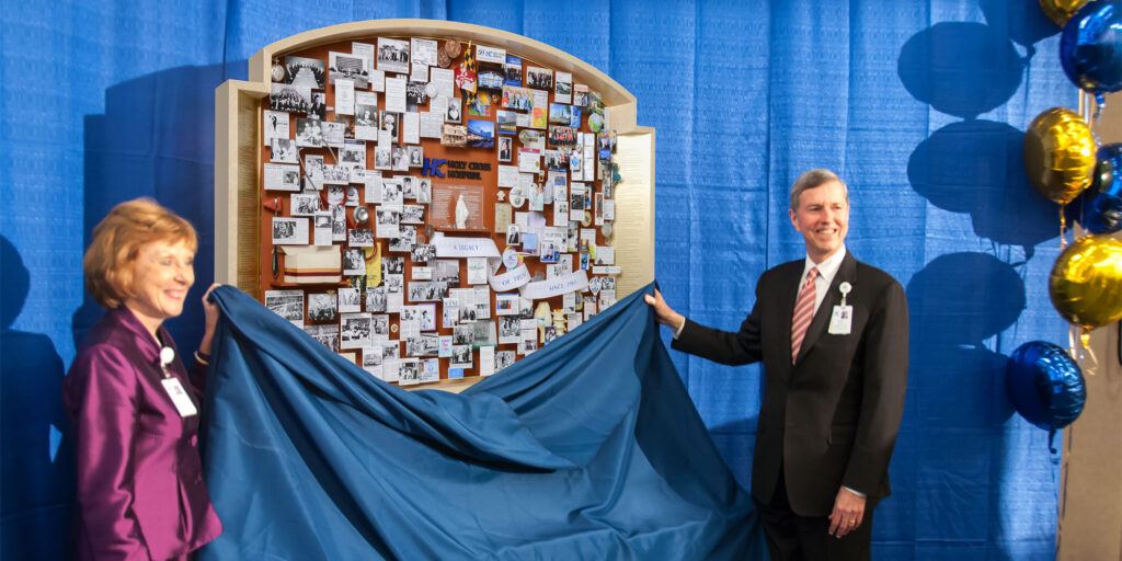 Two people standing next to the Holy Cross collage as a cloth is being removed, revealing the collage to the audience.