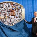 Two people standing next to the Holy Cross collage as a cloth is being removed, revealing the collage to the audience.