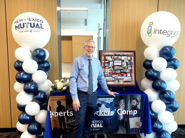 New Mexico Mutual CEO smiling and standing next to shadow box collage commemorating his retirement with balloons on either side