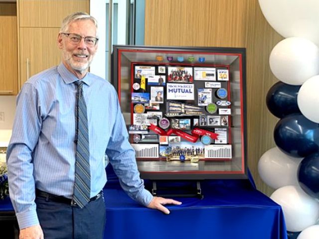 New Mexico Mutual CEO smiling and standing next to shadow box collage commemorating his retirement