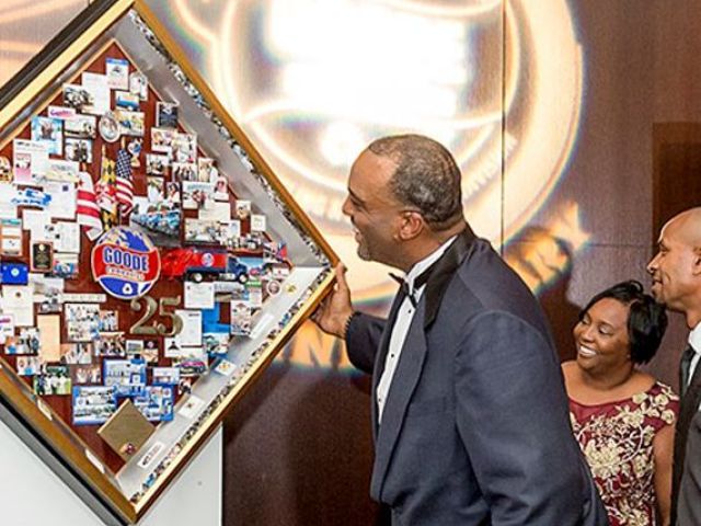 Goode Companies' CEO smiling while looking at a shadow box collage that commemorates their 25th anniversary