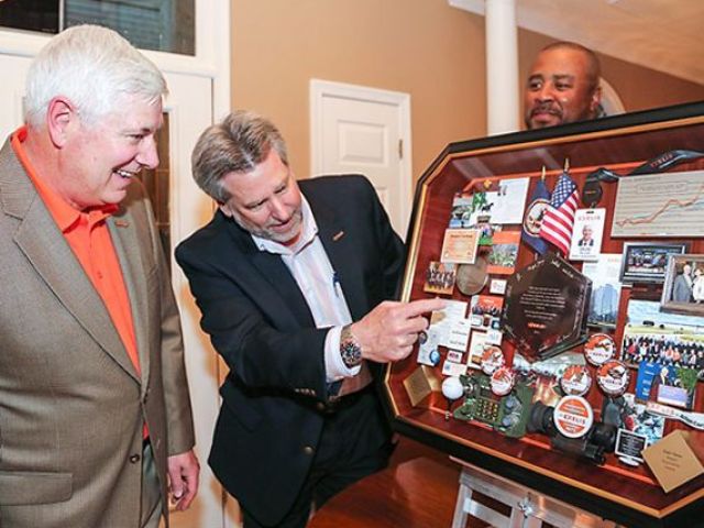 Exelis CEO and others smiling and pointing out items in shadow box collage honoring his career
