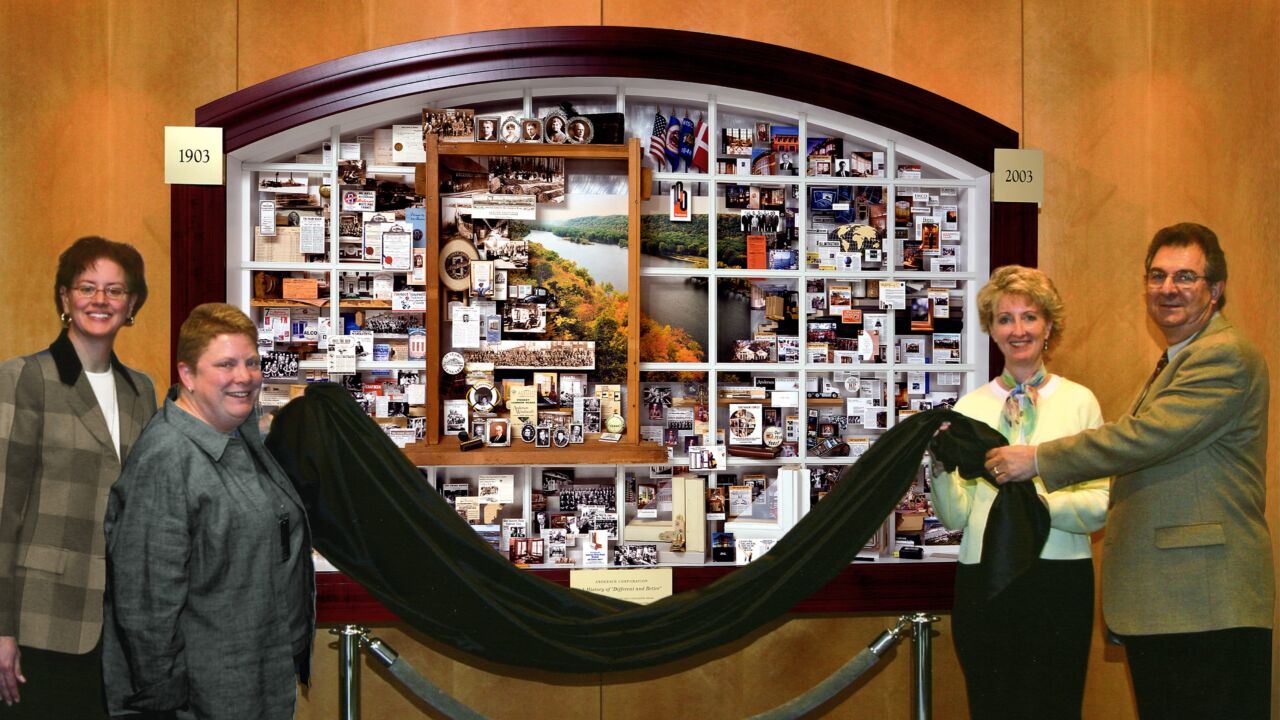 Staff unveiling large shadow box collage on wall for Andersen Windows' 100th Anniversary